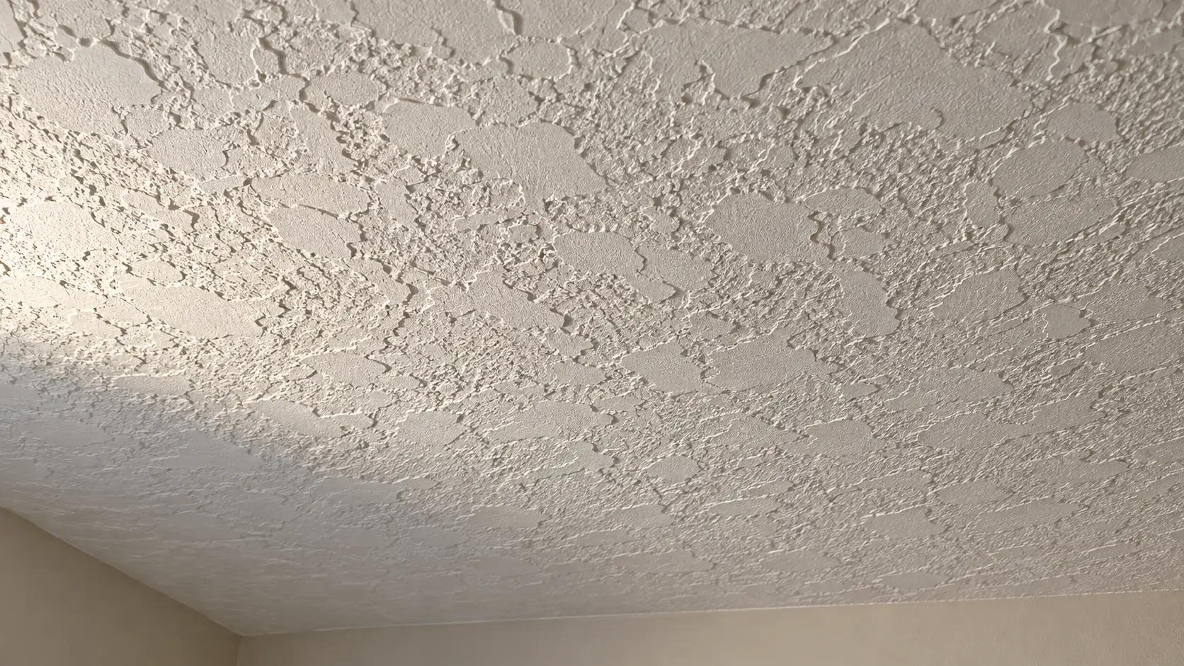 Close-up of a knockdown textured ceiling lit from the side so the flattened peaks and valleys of the texture cast visible shadows